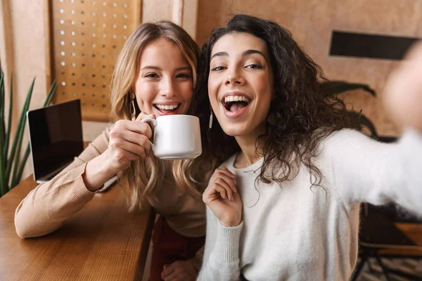 Счастливые, счастливые девушки, сидящие в кафе, делают селфи на камеру. . — стоковое фото