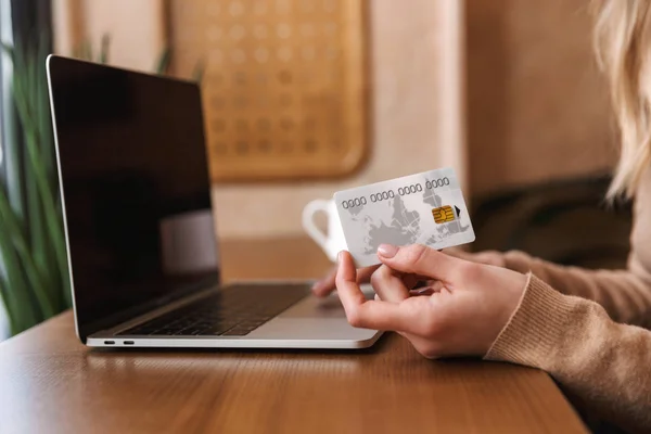 Imagem cortada de menina bonita sentado no café segurando cartão de crédito usando laptop . — Fotografia de Stock