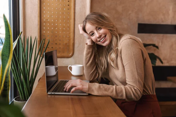 Прекрасная счастливая девушка, сидящая в кафе с ноутбуком . — стоковое фото