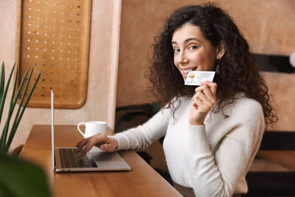 Menina muito emocional sentado no café usando computador portátil segurando cartão de crédito . — Fotografia de Stock