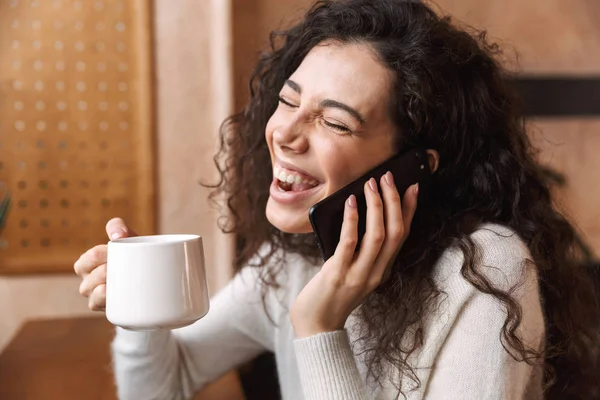 Ziemlich emotionales glückliches Mädchen sitzt im Café und telefoniert. — Stockfoto