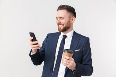 Mutlu işadamı cep telefonu kullanarak kahve içme beyaz duvar arka plan üzerinde izole poz.