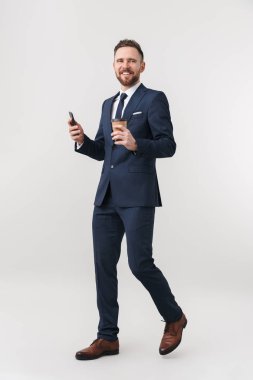 Mutlu işadamı cep telefonu kullanarak kahve içme beyaz duvar arka plan üzerinde izole poz.