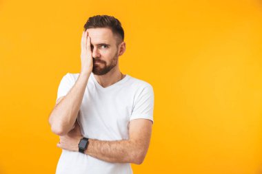 Gözü kaplayan sarı duvar arka planı üzerinde izole poz veren adam.