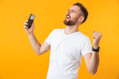 Mutlu genç yakışıklı adam kulaklık ile müzik dinleme cep telefonu kullanarak sarı duvar arka plan üzerinde izole poz.