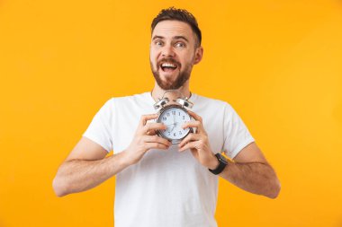 Heyecanlı adam çalar saat tutan sarı duvar arka plan üzerinde izole poz.
