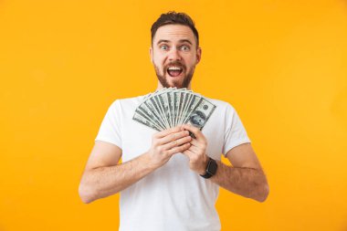 Mutlu genç yakışıklı adam para tutan sarı duvar arka plan üzerinde izole poz.