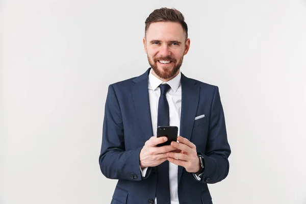 Ευτυχισμένος νέος όμορφος επιχειρηματίας που παρουσιάζουν απομονωμένα πάνω από λευκό τοίχο φόντο χρησιμοποιώντας το κινητό τηλέφωνο. — Φωτογραφία Αρχείου