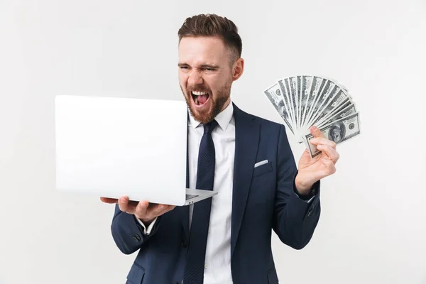 Empresário animado posando isolado sobre fundo parede branca segurando computador portátil e dinheiro . — Fotografia de Stock