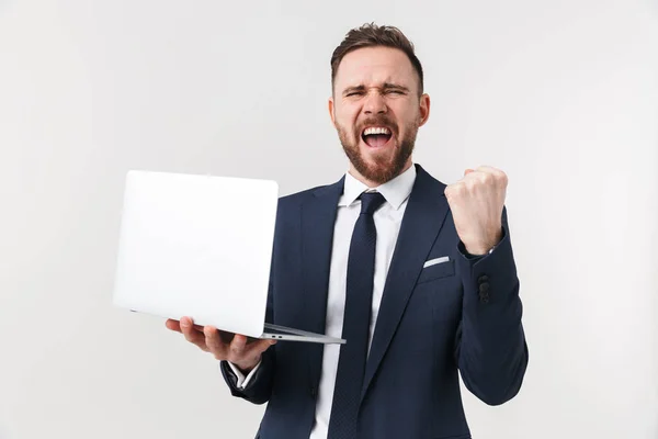 Empresário animado posando isolado sobre fundo da parede branca segurando computador portátil . — Fotografia de Stock