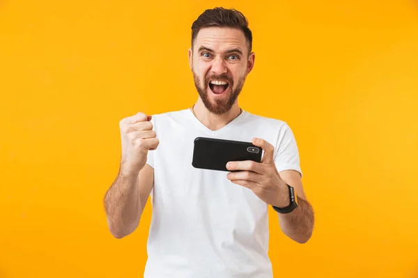 Hhappy man poserar isolerade över gul vägg bakgrund spela spel via telefon. — Stockfoto