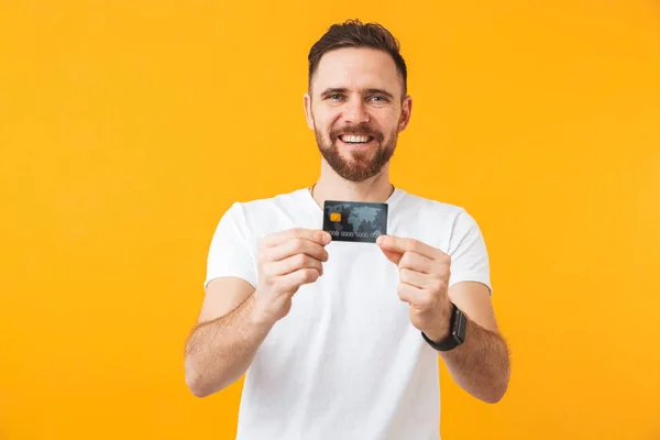 Feliz joven guapo hombre posando aislado sobre fondo amarillo de la pared celebración de la tarjeta de crédito . — Foto de Stock
