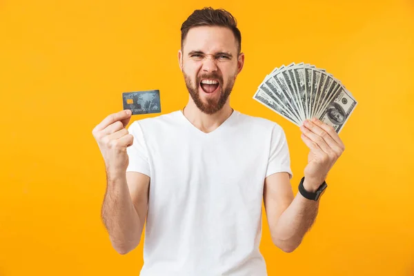 快乐男子摆出孤立在黄墙背景持有金钱和信用卡. — 图库照片
