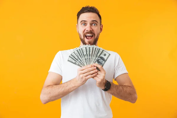 Šťastný mladý pohledný muž, který představuje izolaci na pozadí žluté zdi a drží peníze. — Stock fotografie