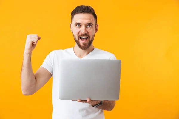 Hombre excitado posando aislado sobre fondo de pared amarillo usando computadora portátil . — Foto de Stock