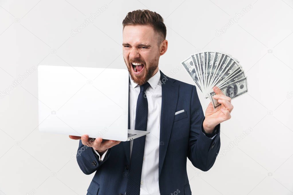 Excited businessman posing isolated over white wall background holding laptop computer and money.