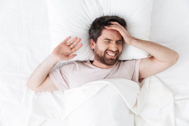 Yatakta battaniye altında sabah baş ağrısı ile yakışıklı genç adam.