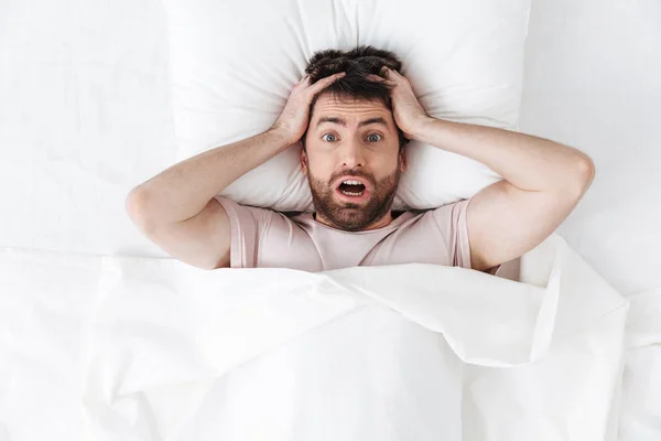 Döbbenve zavaros csinos fiatalember reggel takaró alatt az ágyban. — Stock Fotó