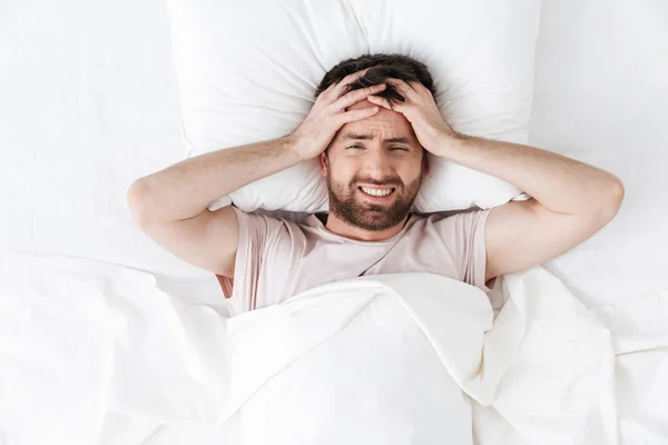 Beau jeune homme avec mal de tête le matin sous couverture au lit . — Photo