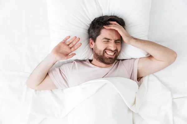 Yatakta battaniye altında sabah baş ağrısı ile yakışıklı genç adam. — Stok fotoğraf