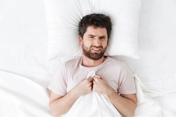Δυσαρεστημένος νεαρός άντρας το πρωί κάτω από κουβέρτα στο κρεβάτι. — Φωτογραφία Αρχείου