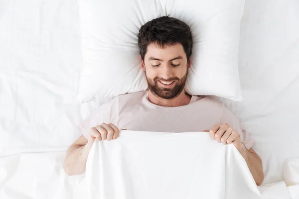 Heureux jeune homme le matin sous couverture au lit se trouve en regardant ses organes génitaux . — Photo