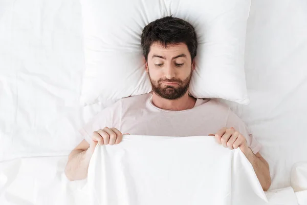 Sabah genç bir adam yatakta battaniyenin altında uzanmış cinsel organına bakıyor.. — Stok fotoğraf