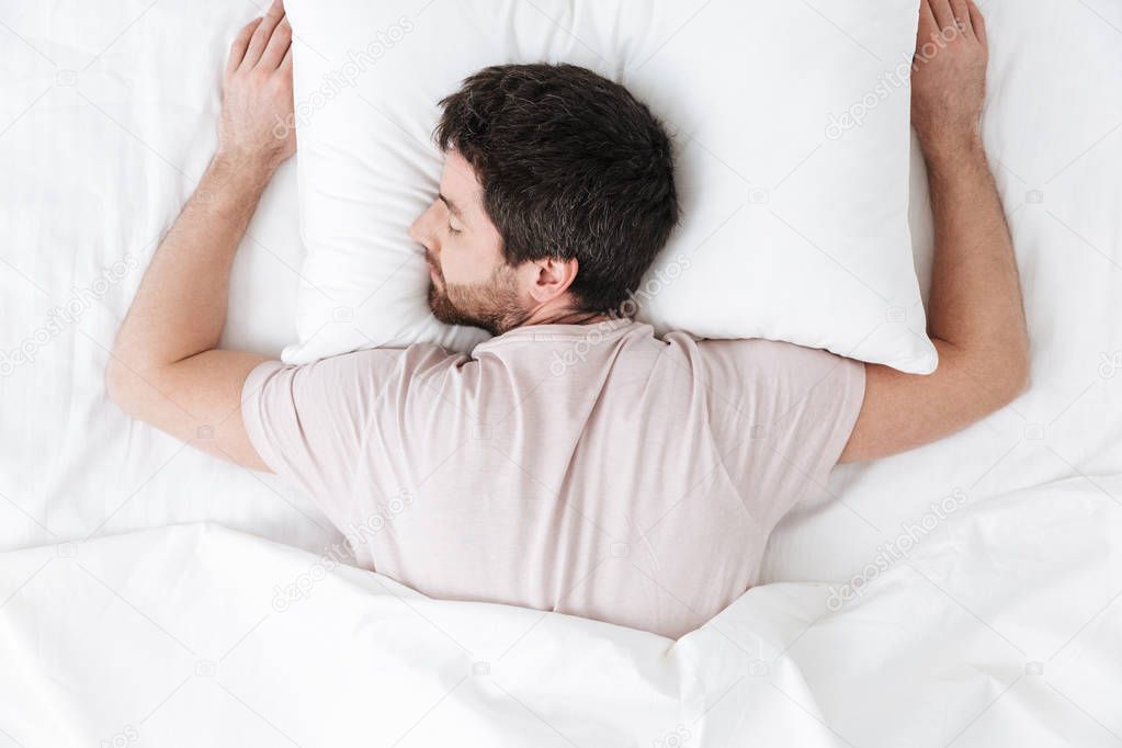 Sleeping young man in the morning under blanket in bed lies.