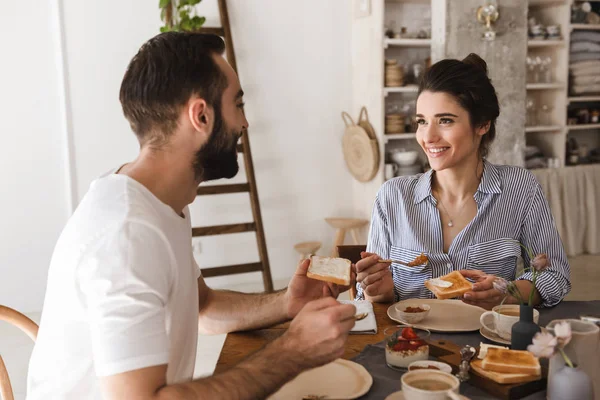 Imagen de la encantadora pareja morena comiendo juntos en la mesa mientras h — Foto de Stock