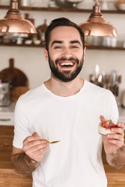 Portrait of joyful brunette man 20s eating panna cotta dessert w — Stock Photo, Image