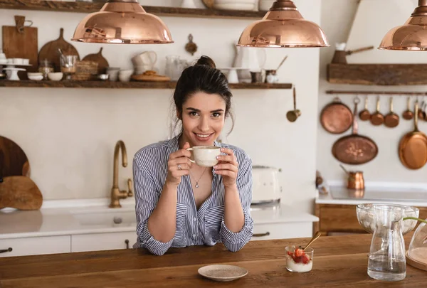Fotó a mosolygó barna nő 20s kávét iszik, miközben — Stock Fotó