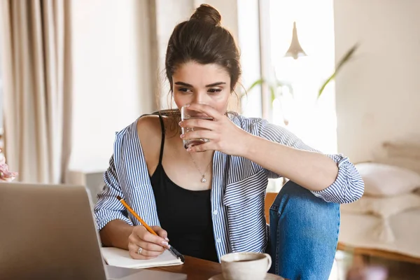 Image of serious pretty woman writing down notes on paper and us