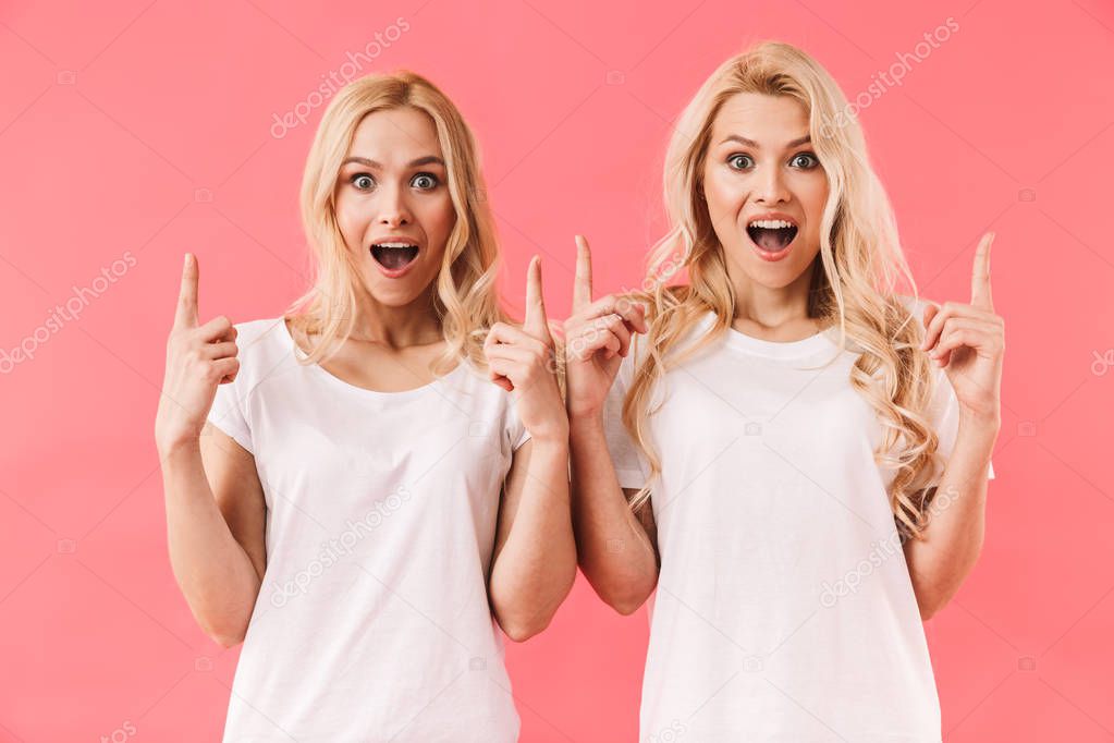 Surprised happy twins wearing in t-shirts pointing up