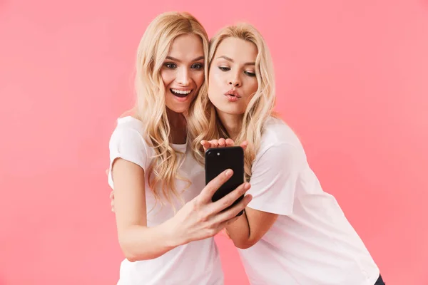 Удивлённые счастливые блондинки-близнецы, одетые в футболки, разговаривающие на видеокассете — стоковое фото
