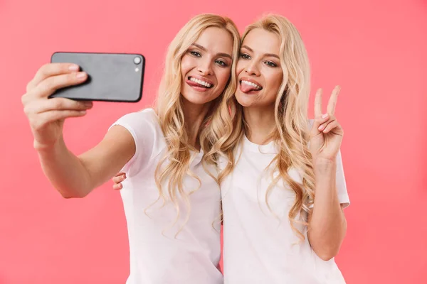 Счастливые блондинки-близнецы в футболках делают селфи на смартфоне — стоковое фото