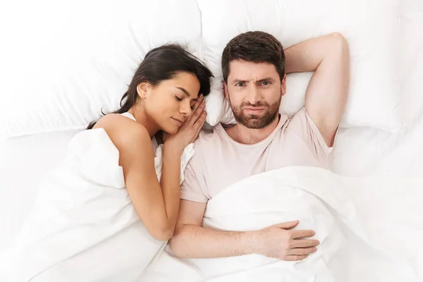 Hoşnutlak şaşkın genç adam uyuyan kadın yakın battaniye altında yatakta yatıyor. — Stok fotoğraf
