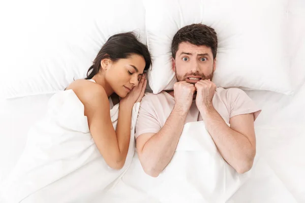 Hoşnutlak şaşkın genç adam uyuyan kadın yakın battaniye altında yatakta yatıyor. — Stok fotoğraf