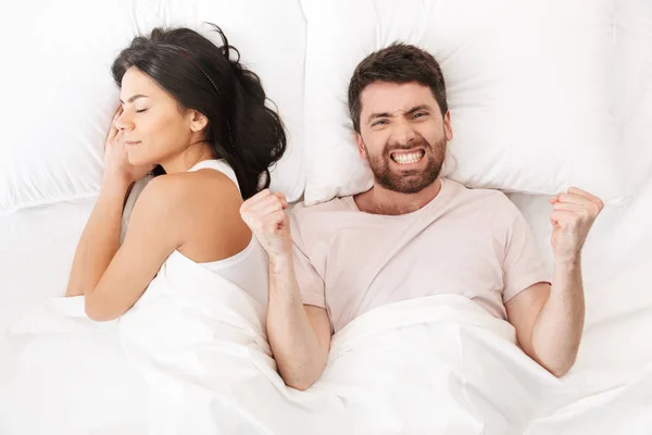 Heyecanlı genç adam uyuyan kadına yakın yatakta battaniye altında yatıyor kazanan jest yapmak. — Stok fotoğraf