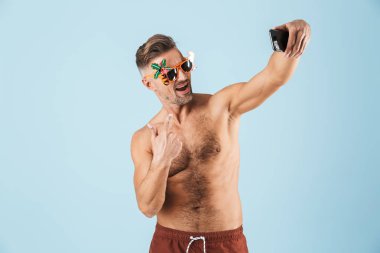Cep telefonu kullanarak mavi duvar arka plan üzerinde yalıtılmış poz mayo heyecanlı mutlu yetişkin adam bir selfie almak.