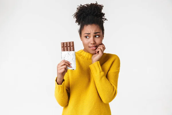 Jovem mulher africana confuso posando isolado sobre fundo da parede branca segurando doces chocolate . — Fotografia de Stock