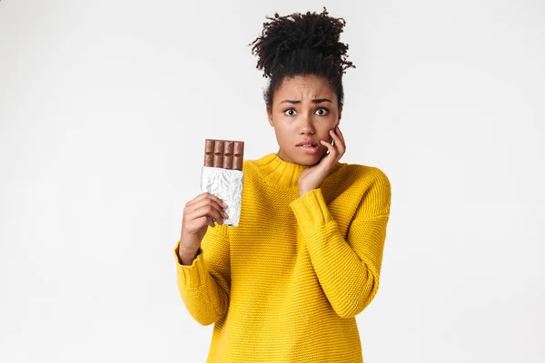 Jovem mulher africana confuso posando isolado sobre fundo da parede branca segurando doces chocolate . — Fotografia de Stock