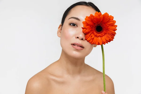 Bonita jovem mulher asiática bonita com pele saudável posando nua isolada sobre fundo de parede branca segurando flor . — Fotografia de Stock