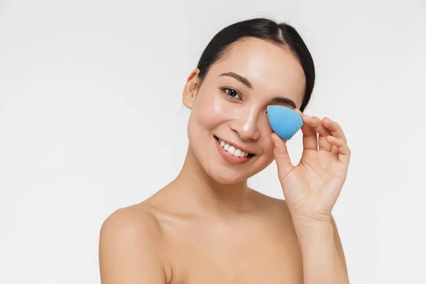 Bastante asiático mujer con saludable piel posando desnudo aislado sobre blanco pared fondo celebración maquillaje esponja . — Foto de Stock