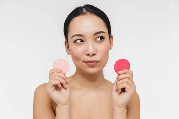 Bastante asiático mujer con saludable piel posando desnudo aislado sobre blanco pared fondo celebración maquillaje esponja . — Foto de Stock