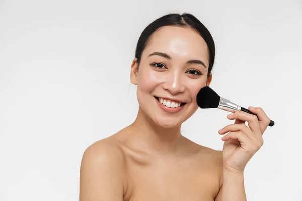 Bastante asiático mujer con saludable piel posando desnudo aislado sobre blanco pared fondo celebración maquillaje cepillo . — Foto de Stock