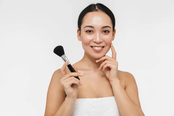 Bastante asiático mujer con saludable piel posando desnudo aislado sobre blanco pared fondo celebración maquillaje cepillo . — Foto de Stock