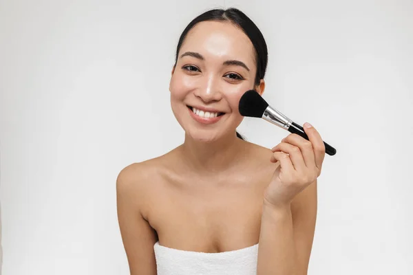 Pretty asian woman with healthy skin posing naked isolated over white wall background holding makeup brush. — Stock Photo, Image