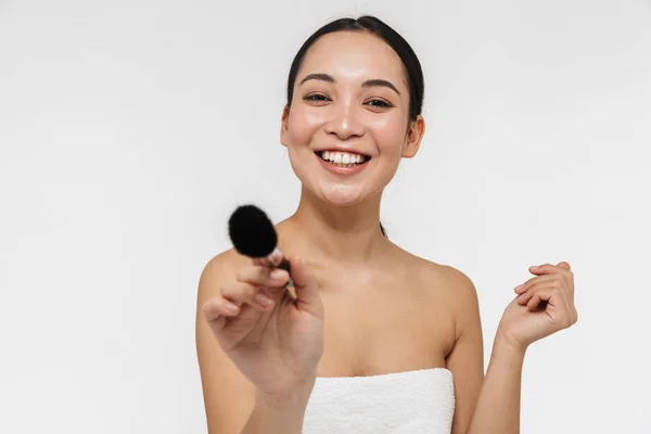 Pretty asiatisk kvinna med frisk hud poserar naken isolerad över vit vägg bakgrund håller makeup borste. — Stockfoto