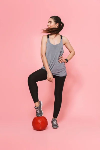 Mooie jonge mooie fitness vrouw poseren met bal geïsoleerd over roze muur achtergrond. — Stockfoto