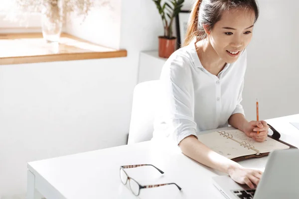 Sorrindo asiático mulher de negócios escrevendo algo e usando computador portátil — Fotografia de Stock